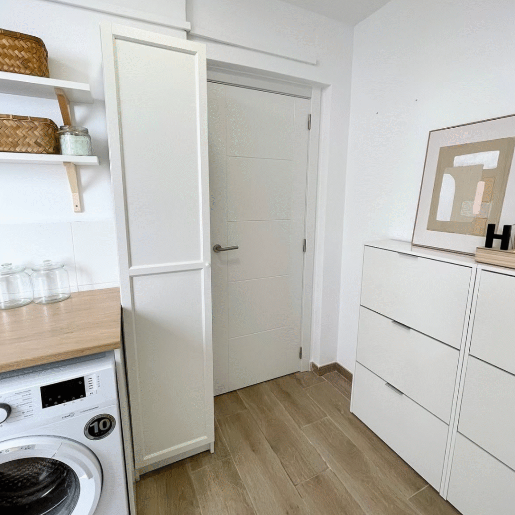 Después de reforma de lavandería pequeña con muebles blancos, pared despejada y almacenaje integrado.